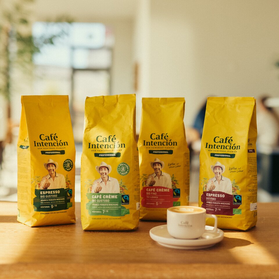 Koffiezakjes van Café Intención worden tentoongesteld naast een kopje espresso in een lichte caféomgeving, waarbij de nadruk ligt op fairtradekoffie.