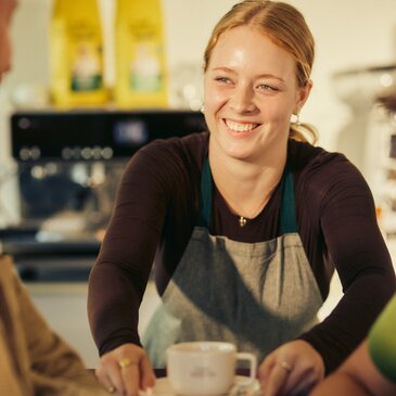 Barista serwujący kawę z uśmiechem w tętniącej życiem kawiarni, podkreślający ciepłą i przyjazną atmosferę.