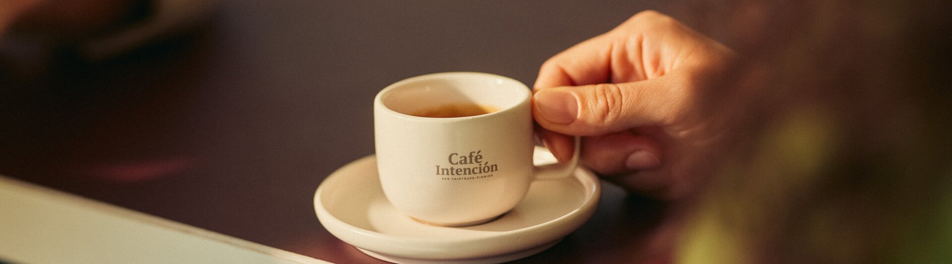 Op een tafel staat een kopje koffie van Café Intención in een hand, wat de gezellige sfeer van het café benadrukt.