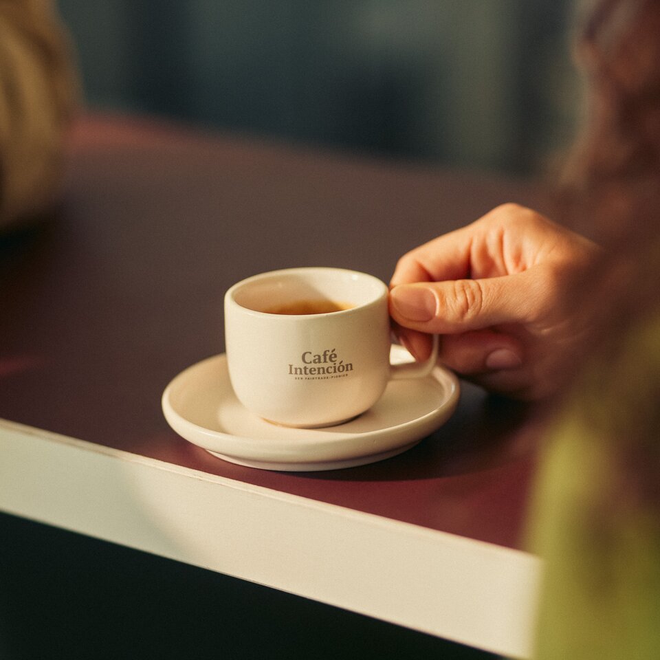 Op een tafel staat een kopje koffie van Café Intención in een hand, wat de gezellige sfeer van het café benadrukt.
